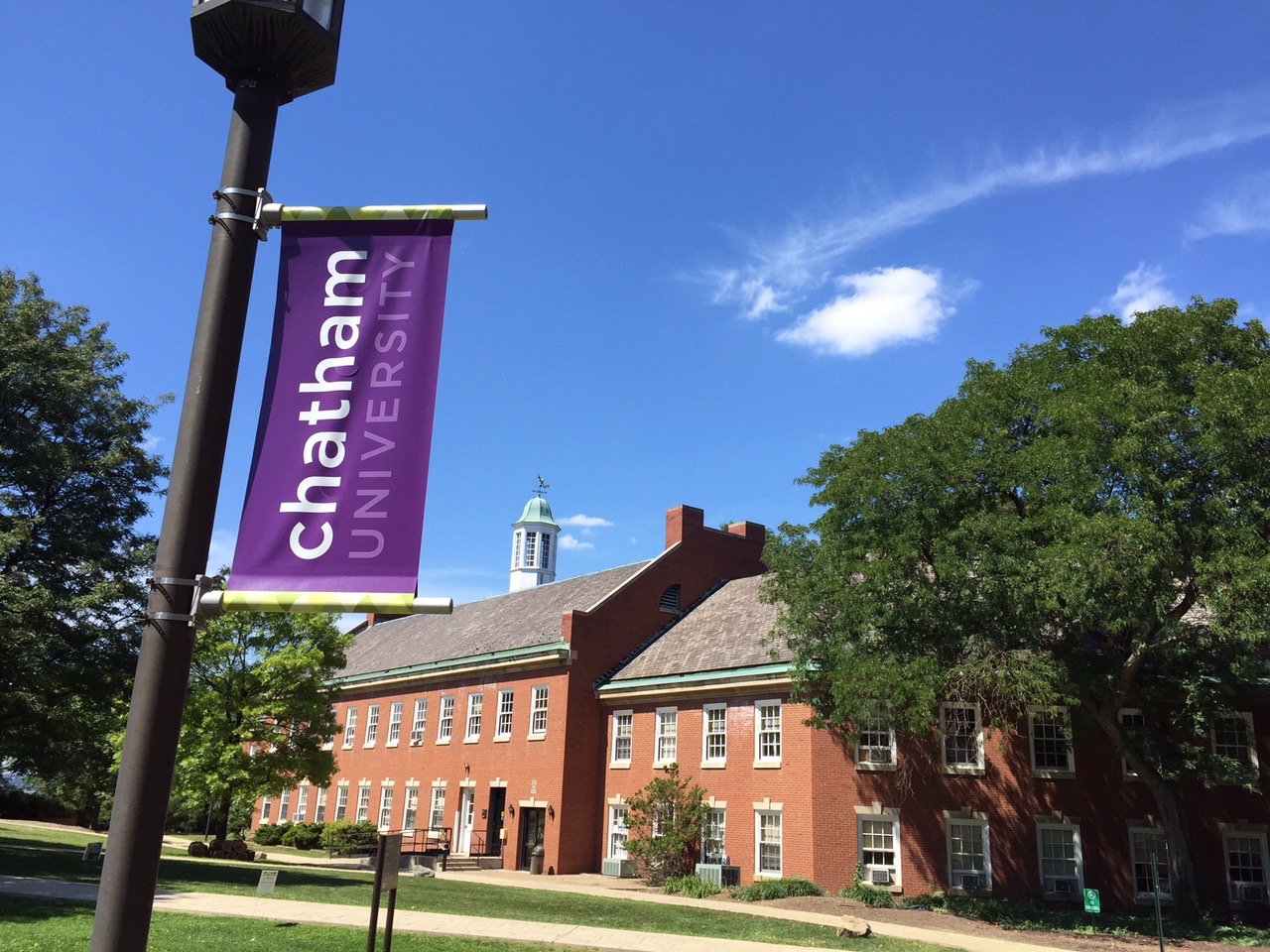 a red brick building with a copper cupola sits behind a banner for Chatham University